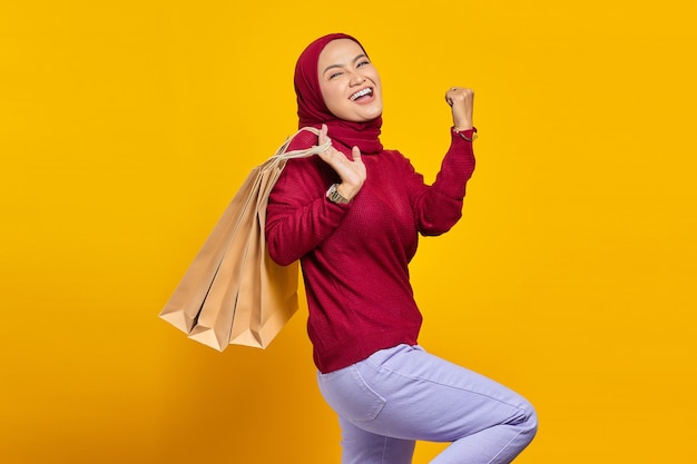 Jeune femme asiatique excitée et joyeuse tenant des sacs à provisions sur fond jaune