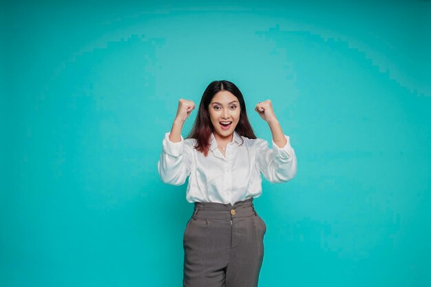 Une jeune femme asiatique avec une expression heureuse et réussie portant une chemise blanche isolée par un fond bleu