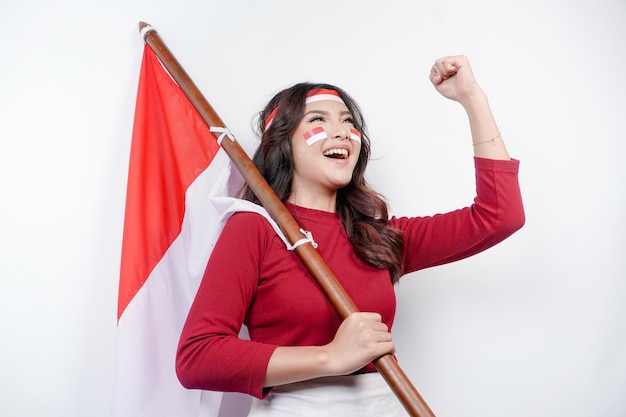 Une jeune femme asiatique avec une expression heureuse et réussie portant un haut rouge et un bandeau sur la tête tout en tenant le drapeau de l'Indonésie isolé par un fond blanc Concept du jour de l'indépendance de l' Indonésie