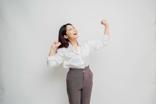 Une jeune femme asiatique avec une expression réussie heureuse portant une chemise blanche isolée par fond blanc