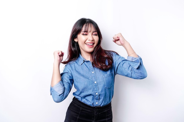 Une jeune femme asiatique avec une expression réussie heureuse portant une chemise bleue isolée par fond blanc