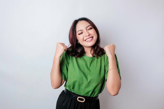 Une jeune femme asiatique avec une expression réussie heureuse portant une chemise verte isolée par fond blanc