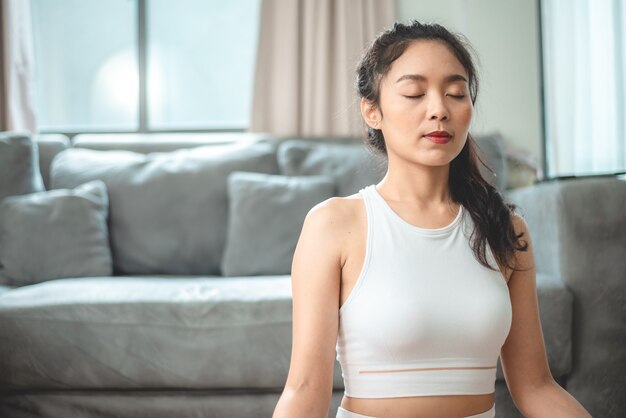 Jeune femme asiatique faisant de l'exercice par yoga à la salle de gym à domicile, mode de vie féminin sain avec entraînement sportif de remise en forme à la maison, fille faisant de l'exercice physique actif du corps salle intérieure de la maison, relaxation et bien-être