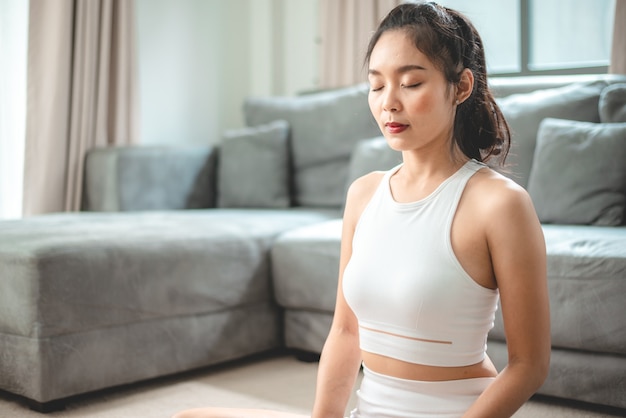 Jeune femme asiatique faisant de l'exercice par yoga à la salle de gym à domicile, mode de vie féminin sain avec entraînement sportif de remise en forme à la maison, fille faisant de l'exercice physique actif du corps salle intérieure de la maison, relaxation et bien-être