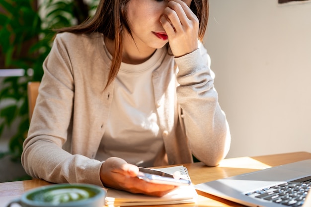 Jeune femme asiatique fatiguée assise dans un café travaillant avec son ordinateur portable et une tasse de café