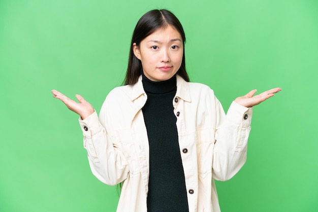 Jeune femme asiatique sur fond de clé chroma isolé ayant des doutes tout en levant les mains
