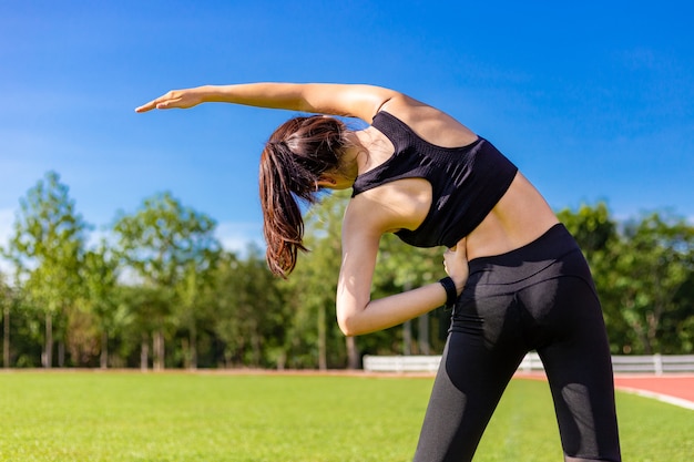 Jeune femme asiatique en forme qui s'étend de son corps pendant son exercice du matin sur une piste de course en plein air