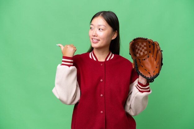 Jeune femme asiatique avec un gant de baseball sur fond isolé pointant vers le côté pour présenter un produit