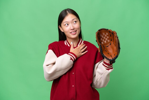 Jeune femme asiatique avec un gant de baseball sur fond isolé regardant en souriant