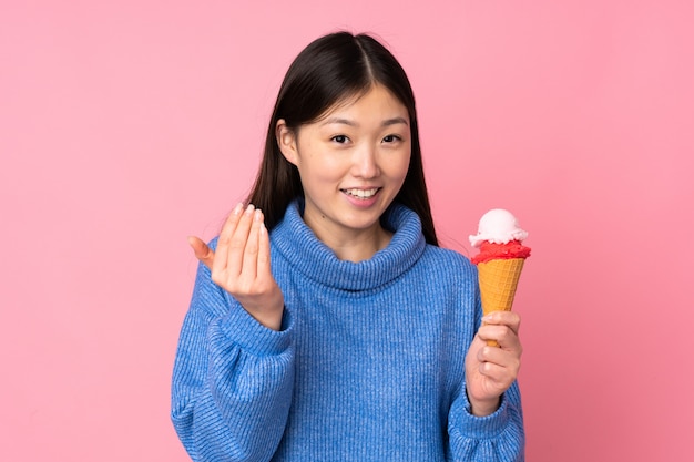 Jeune femme asiatique avec une glace sur le mur rose invitant à venir avec la main