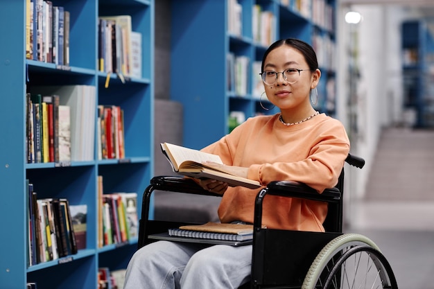 Jeune femme asiatique handicapée dans la bibliothèque souriant à la caméra