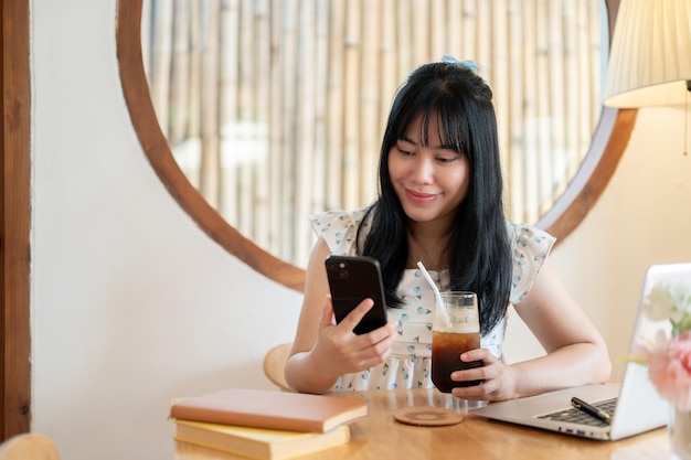 Une jeune femme asiatique heureuse et charmante se détend dans un café et utilise son smartphone.