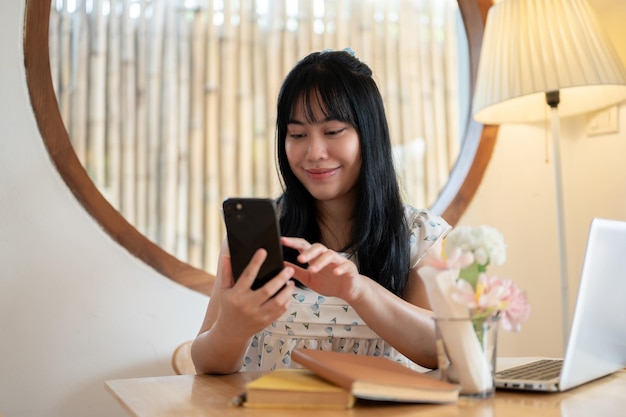 Une jeune femme asiatique heureuse et charmante se détend dans un café et utilise son smartphone.