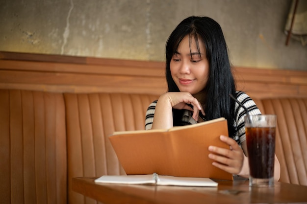 Une jeune femme asiatique heureuse lit un livre ou fait ses devoirs dans un beau café vintage.