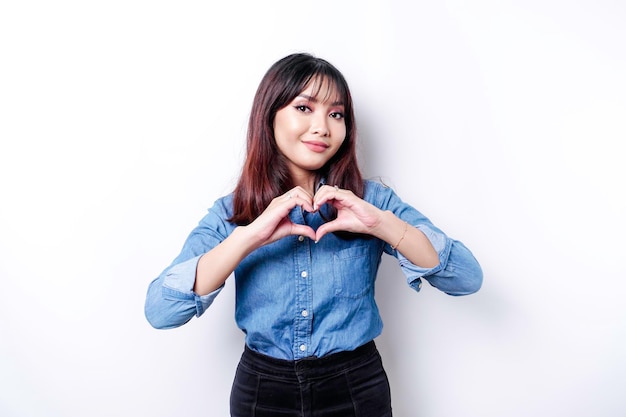 Une jeune femme asiatique heureuse portant une chemise bleue sent des formes romantiques le geste du cœur exprime des sentiments tendres