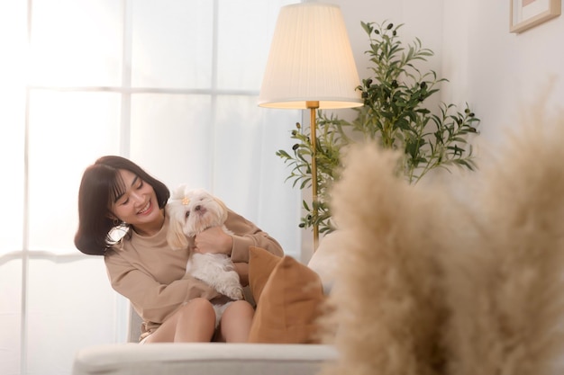 Une jeune femme asiatique heureuse qui caresse et passe du temps avec un mignon chien dans le salon.