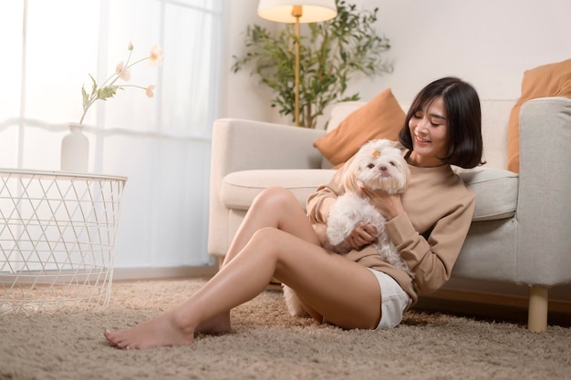 Une jeune femme asiatique heureuse qui caresse et passe du temps avec un mignon chien dans le salon.