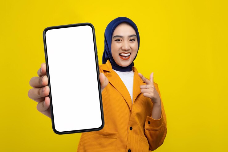Une jeune femme asiatique heureuse tenant un smartphone avec un écran vide et souriante isolée sur un fond jaune