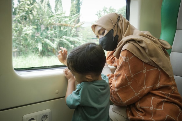 Une jeune femme asiatique en hijab et son fils parlent et regardent par la fenêtre à l'intérieur du train