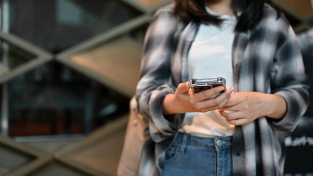 Une jeune femme asiatique hipster dans une chemise en flanelle utilise son smartphone dans le centre commercial