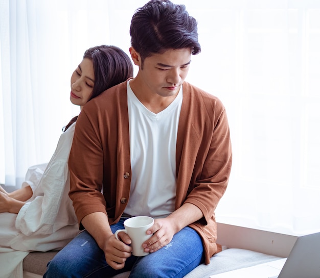 Jeune femme asiatique et homme à la maison avec une tasse de café dans les mains.