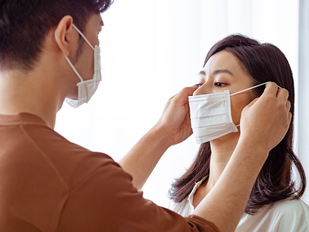 Jeune femme asiatique et homme portant un masque chirurgical à la maison