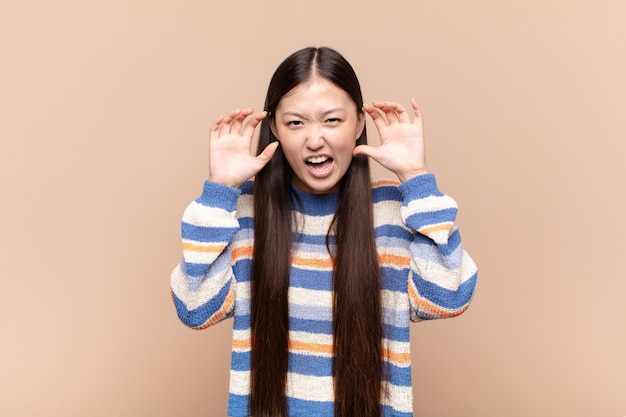 Jeune femme asiatique hurlant de panique ou de colère, choquée, terrifiée ou furieuse, avec les mains à côté de la tête