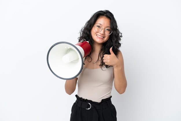 Jeune femme asiatique isolée sur fond blanc tenant un mégaphone avec le pouce vers le haut