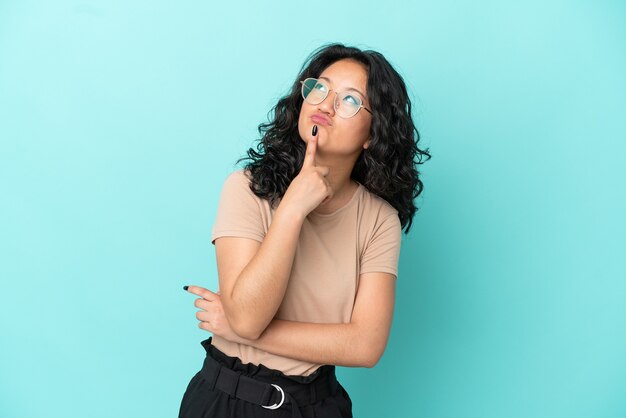 Jeune femme asiatique isolée sur fond bleu ayant des doutes en levant les yeux