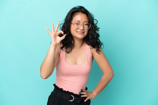 Jeune femme asiatique isolée sur fond bleu montrant un signe ok avec les doigts