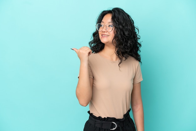 Jeune femme asiatique isolée sur fond bleu pointant vers le côté pour présenter un produit