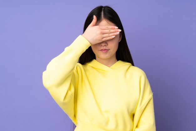 Jeune femme asiatique isolée sur fond violet couvrant les yeux par les mains