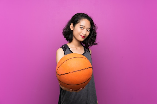 Jeune femme asiatique jouant au basketball sur mur violet