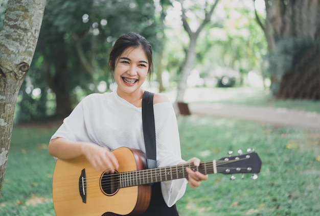 Jeune femme asiatique jouant de la guitare et chanter de la musique dans le parc