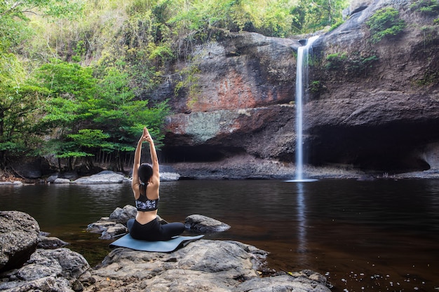 Une jeune femme asiatique joue au yoga devant la cascade.