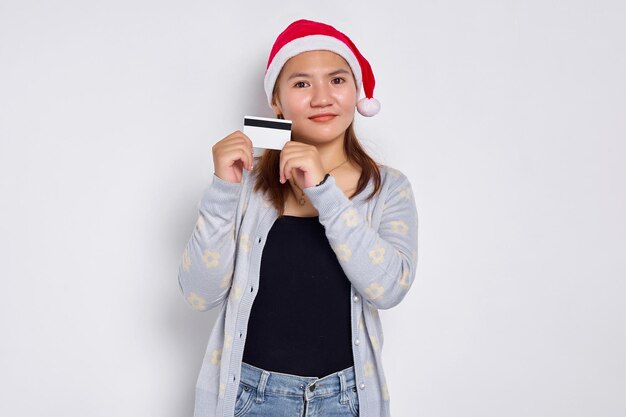 Jeune femme asiatique joyeuse et excitée dans un chapeau de Noël montrant une carte de crédit blanche vierge à la caméra isolée sur fond blanc