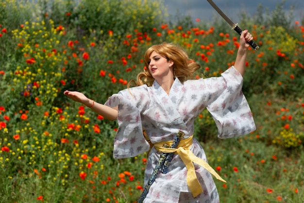 Une jeune femme asiatique en kimono traditionnel entraîne des techniques de combat avec une épée katana sur les collines avec des coquelicots rouges, une fille guerrière samouraï