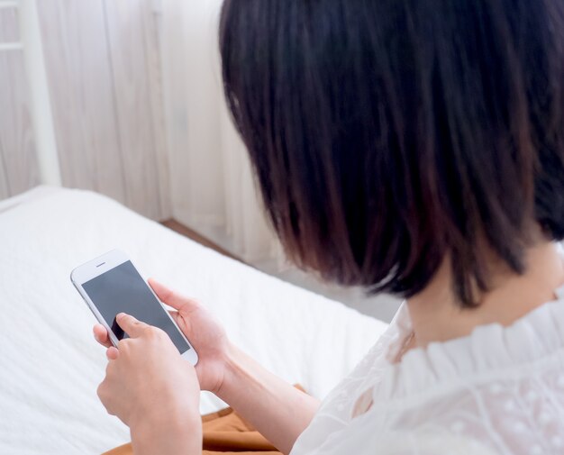 Jeune femme asiatique sur le lit à l'aide de téléphone