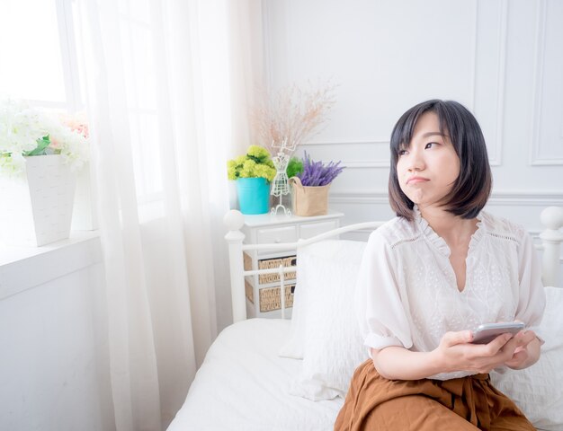 Jeune femme asiatique sur le lit à l'aide de téléphone