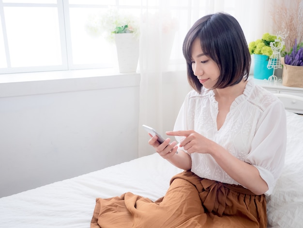 Jeune femme asiatique sur le lit à l'aide de téléphone