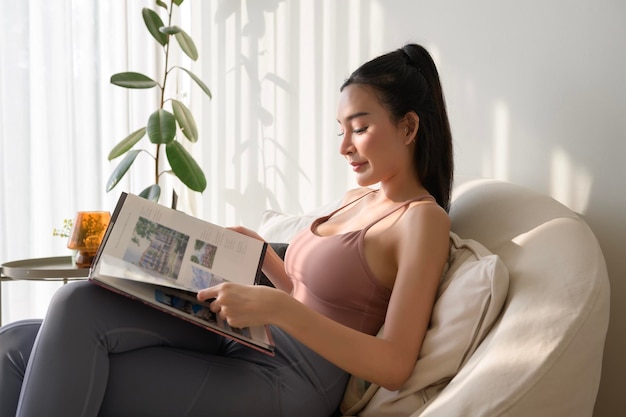 Photo une jeune femme asiatique lit un livre dans le salon à la maison.