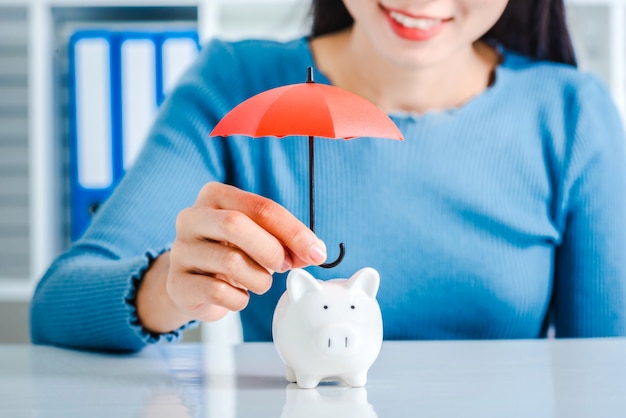 Jeune femme asiatique main tenir parapluie jouet pour protéger la tirelire.