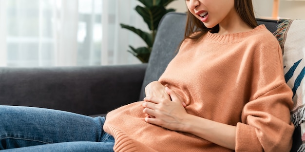 Jeune femme asiatique mains tenant l'estomac et les crampes de la période douloureuse parce qu'elle a ses règles.