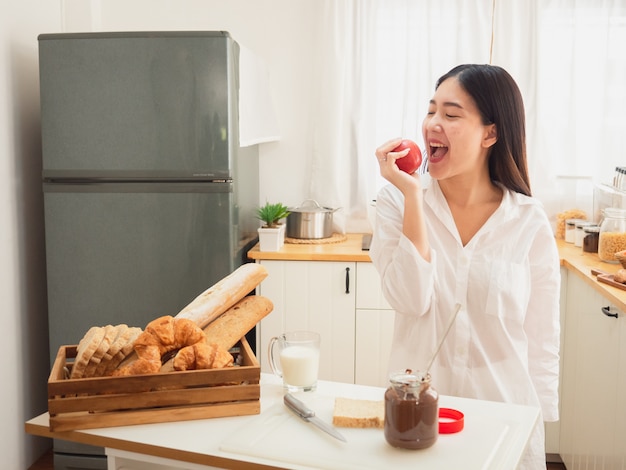 Jeune femme asiatique mange une pomme dans la cuisine