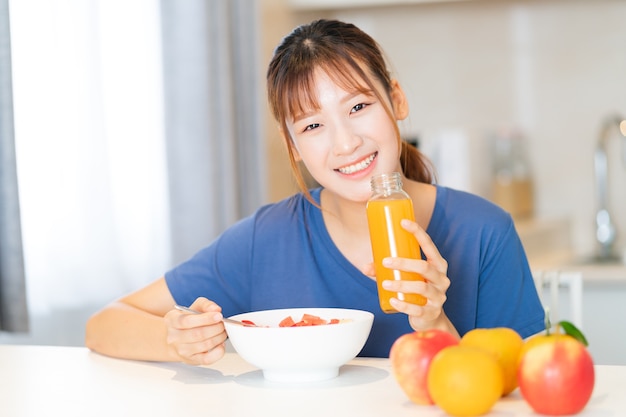 Une jeune femme asiatique mangeant le petit déjeuner avec des fruits dans sa cuisine