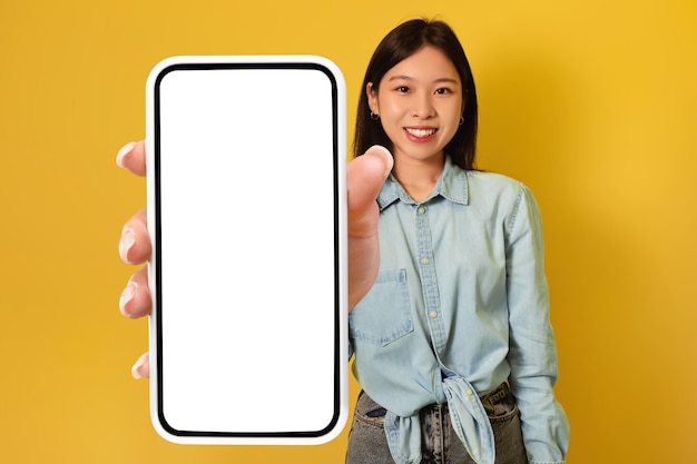 Jeune femme asiatique montrant un grand smartphone avec une maquette faisant la promotion d'une application ou d'un site Web ou d'un produit publicitaire