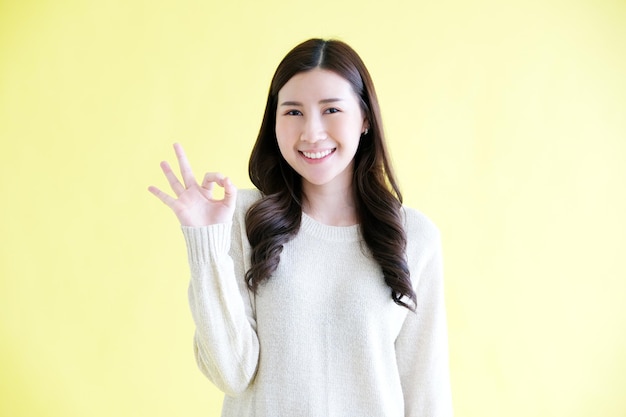 Jeune femme asiatique montrant le signe de la main ok en se tenant debout sur fond jaune isolé