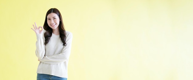 Jeune femme asiatique montrant le signe de la main ok en se tenant debout sur fond jaune isolé