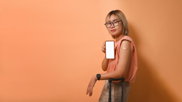 Jeune femme asiatique montrant un téléphone intelligent et un bras vacciné