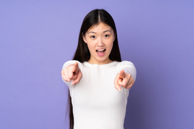 Jeune femme asiatique sur mur violet surpris et pointant vers l'avant